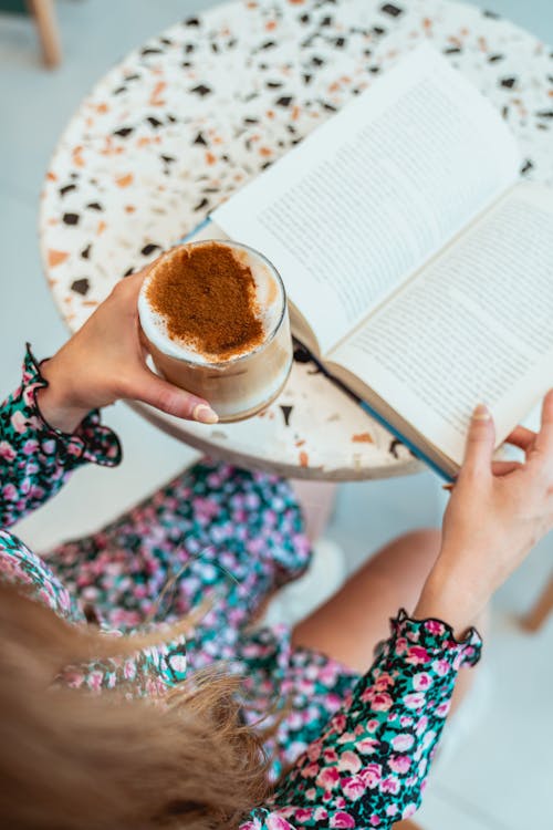 Photo of Woman Reading Book while Holding Iced Latte