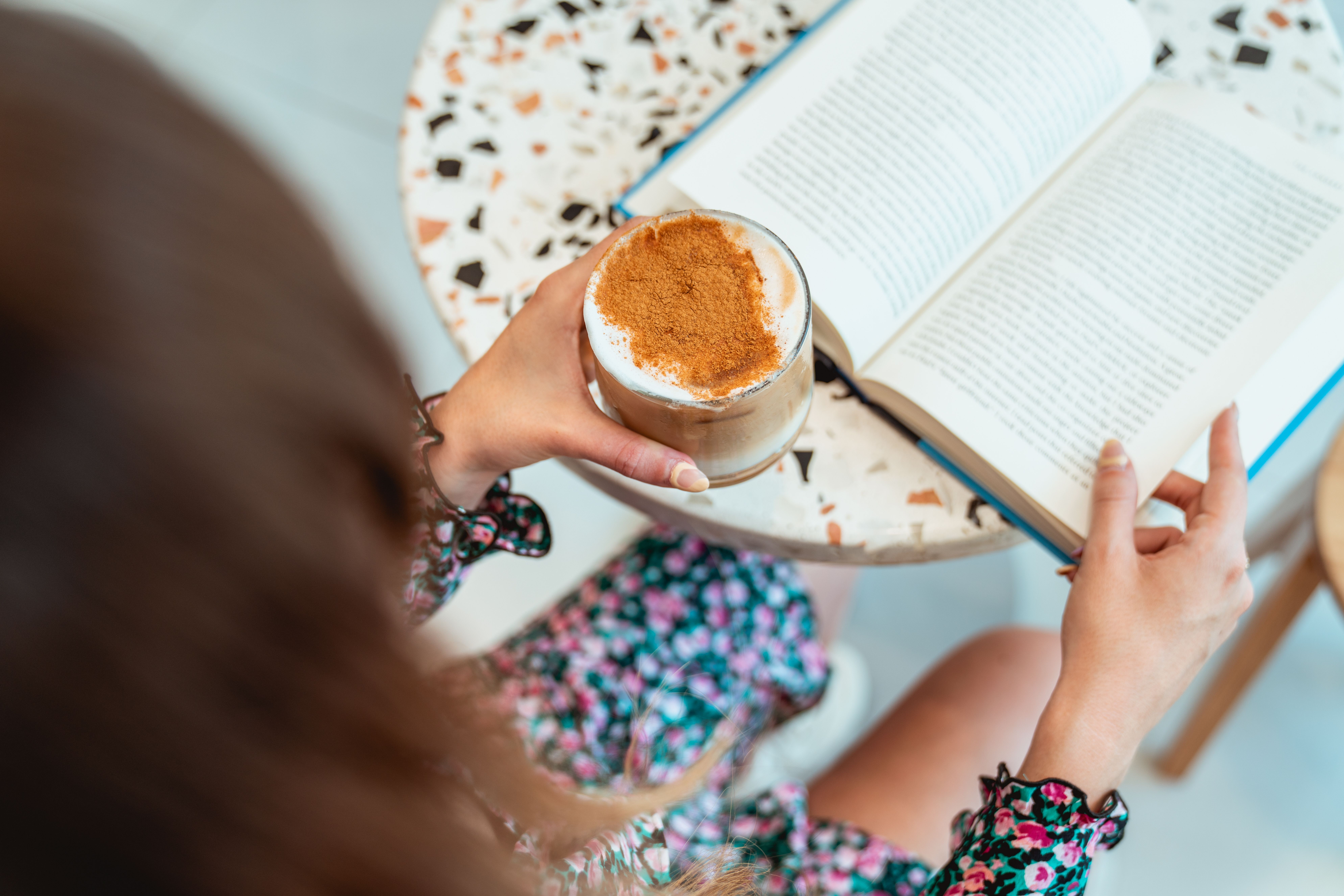 A person enjoys a cappuccino while reading a book in a stylish cafe setting.
