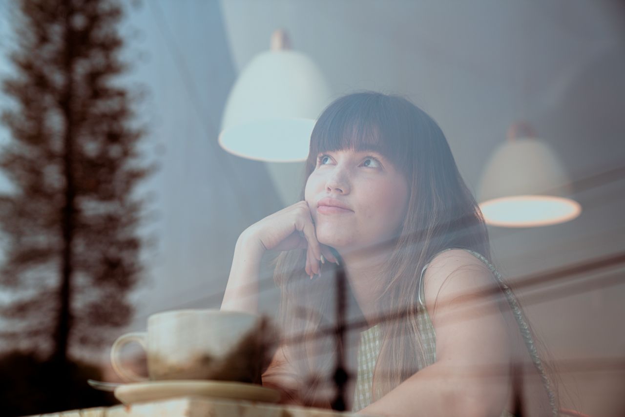 thoughtful woman gazing outside a caf window with reflections and warm