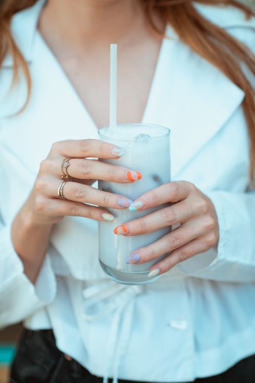 Free A woman with colorful nails holds a glass of coconut juice with a straw, showcasing refreshing beverage in a cafe setting. Stock Photo