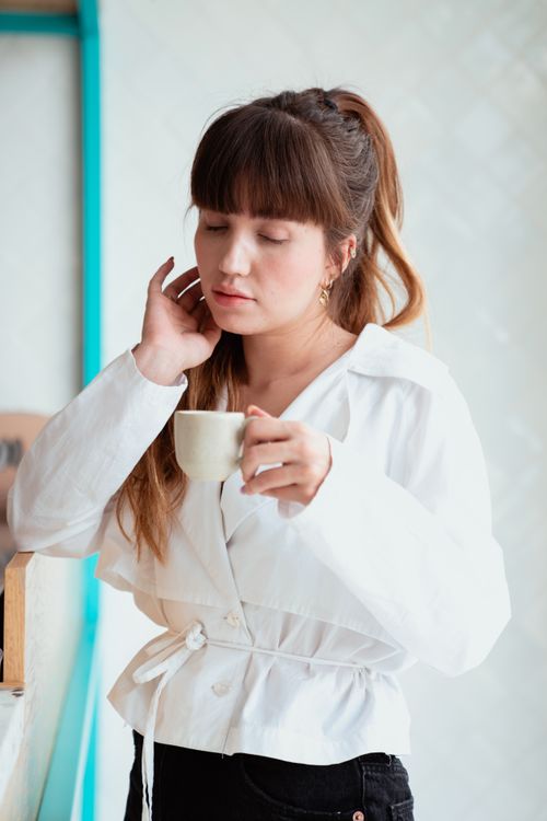 Free A woman in a white shirt enjoys a moment with a coffee cup in a cozy indoor setting. Stock Photo
