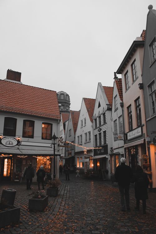 Free Charming cobbled street in a European town under overcast skies, people strolling by historic buildings. Stock Photo