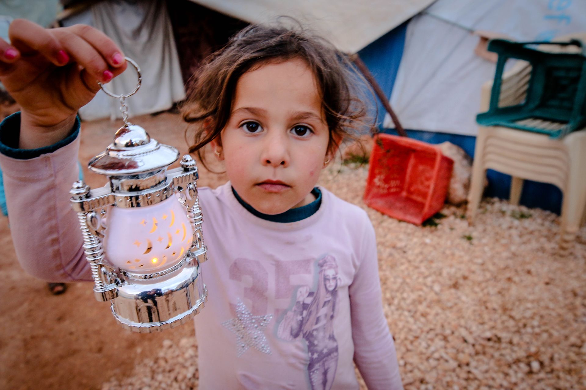 Child in a Syrian refugee camp holding a decorative lantern, showcasing resilience.