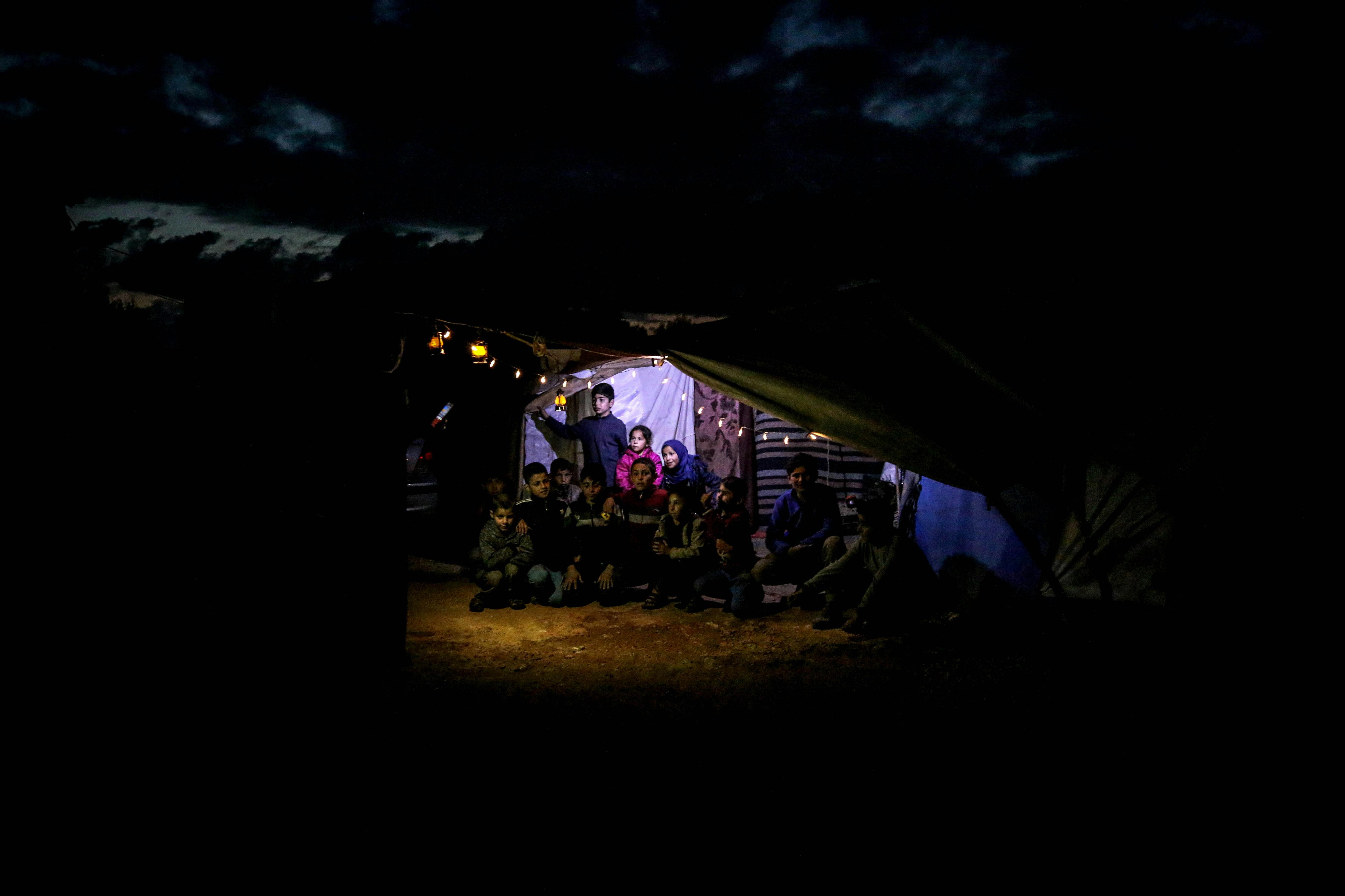 Group of children gathered inside a lit tent at night, illuminated by string lights