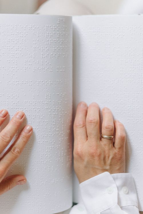 Free Hands touch and read text on a Braille book page. Inclusive reading. Stock Photo