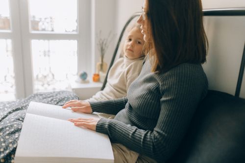 Free A woman and child reading a braille book in a cozy bedroom setting, enhancing child development. Stock Photo