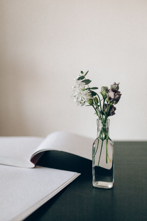 Free A minimalist still life featuring a vase with flowers and an open braille book on a table. Stock Photo