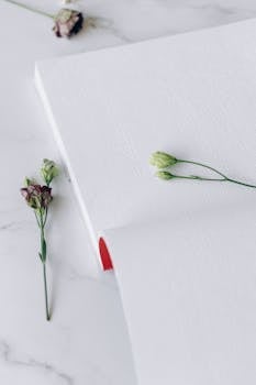 Flat lay view of an open Braille book with delicate flowers on a marble surface, highlighting tactile reading.