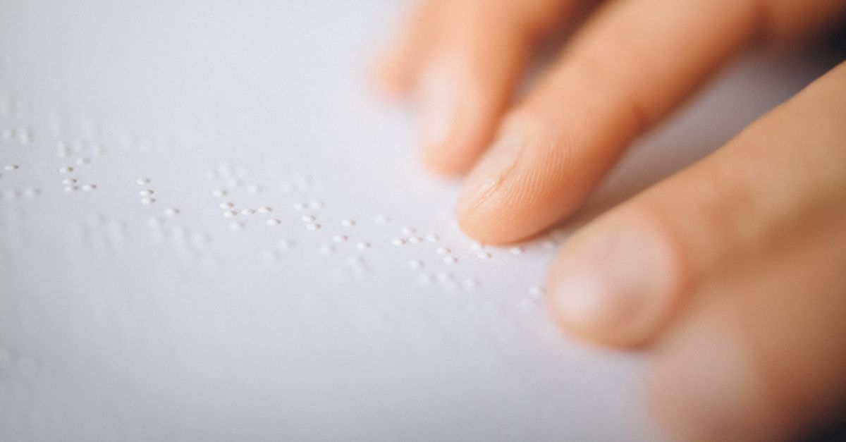 A close-up image of fingers touching and reading a Braille book for sensory perception.