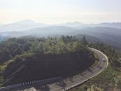 从空中俯瞰，泰国清迈一条蜿蜒的道路穿过郁郁葱葱的森林，背景是薄雾笼罩的山脉