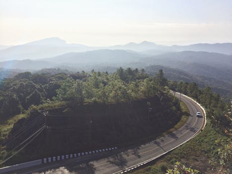 Aerial view of a winding road through lush green forest with misty mountain backdrop in Chiang Mai, Thailand.