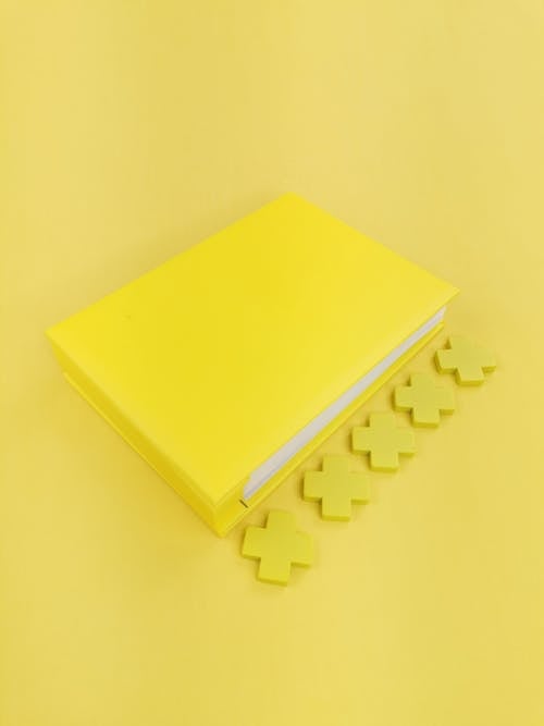 Composition of closed bright yellow notepad with yellow crosses placed on centre of light yellow background