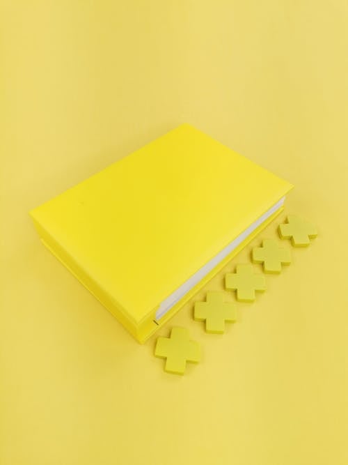 Free Composition of closed bright yellow notepad with yellow crosses placed on centre of light yellow background Stock Photo