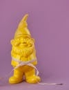 Composition of measuring tape on bright yellow garden gnome placed on left side on light purple surface