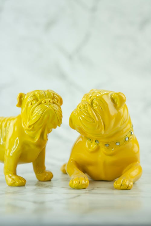 Closeup composition of small bright yellow ceramic toy bulldogs with dog collar on white marble background