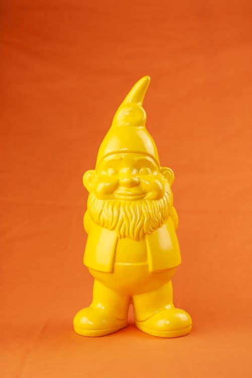 Small bright yellow garden gnome with beard and hat standing on centre of orange background