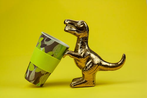 Souvenir in form of gilded shiny dinosaur with tilted cup composed on yellow background