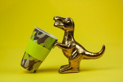 Free Souvenir in form of gilded shiny dinosaur with tilted cup composed on yellow background Stock Photo