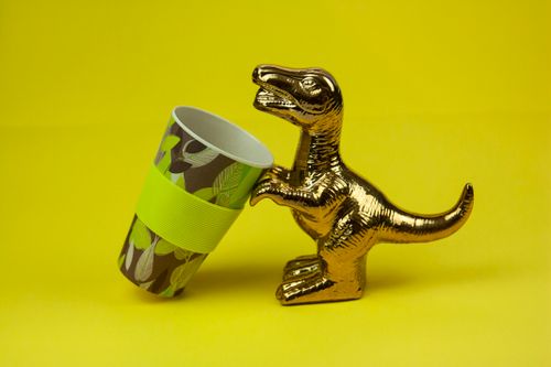 Free Isolated statuette of gilded glowing dinosaur drinking from ceramic cup against yellow background Stock Photo