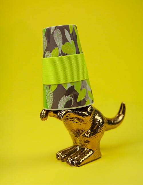 Statuette of shiny gilded animal with mug put on head against yellow background