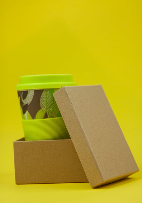 Green cup with lid placed in paper eco friendly box against yellow background