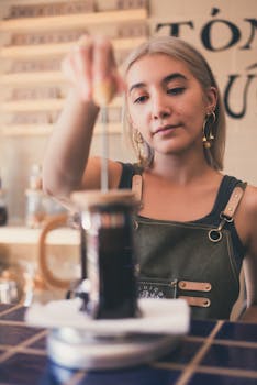 Barista using a French press to make coffee in a trendy café setting.