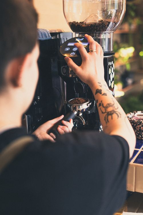 Free A tattooed barista adjusts the settings on a coffee grinder in a trendy cafe. Stock Photo