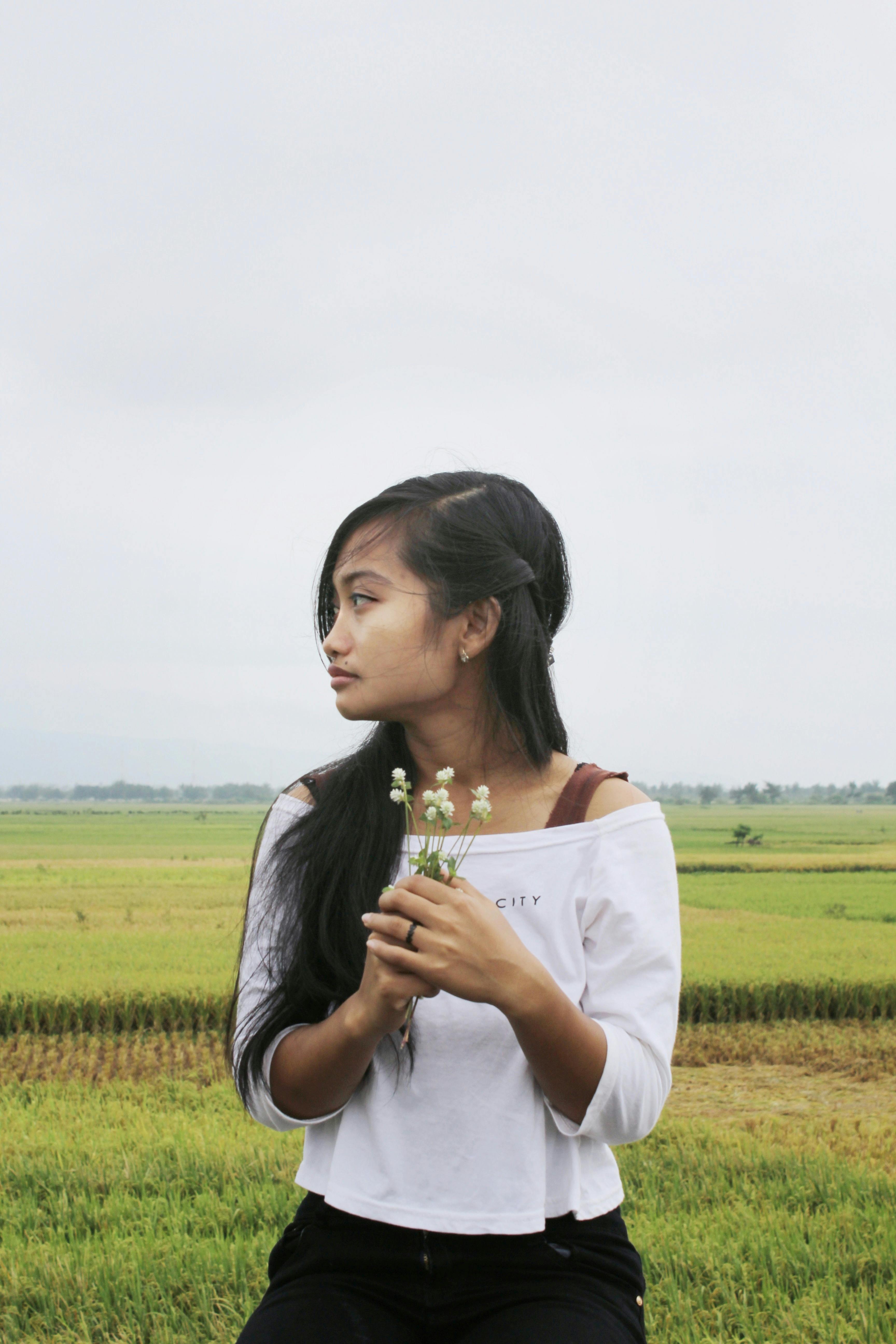 一位年轻女子手持鲜花，站在宁静的稻田中