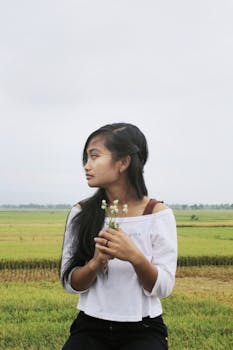 一位年轻女子手持鲜花，站在宁静的稻田中