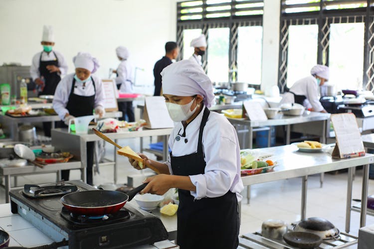 Chefs Cooking In A Kitchen While Wearing Face Masks