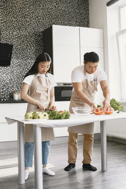 Free Asian couple preparing healthy meals together in a modern kitchen, highlighting teamwork and healthy living. Stock Photo