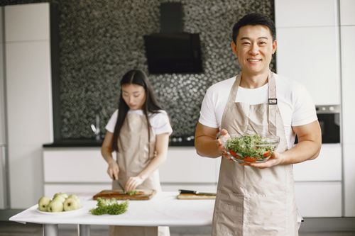 Free Asian couple in a modern kitchen, preparing a fresh salad with vegetables and herbs. Stock Photo