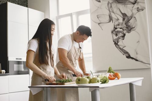 Free Asian couple preparing vegetables indoors together in a bright kitchen. Stock Photo
