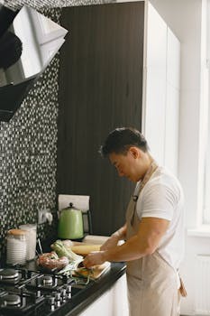 Asian man slicing vegetables in a contemporary kitchen setting, wearing an apron.