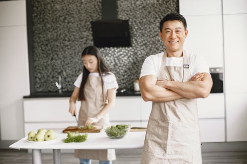 Free Smiling chef in apron stands confidently in a modern kitchen with a woman preparing food. Stock Photo