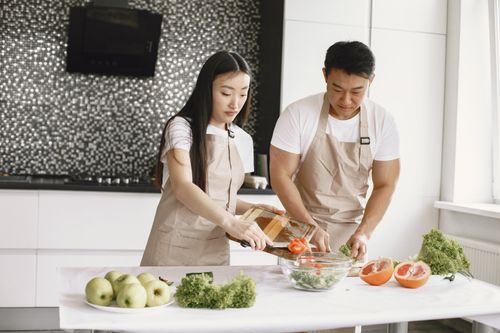 Free Asian couple making a healthy salad together at home in a modern kitchen setting. Stock Photo