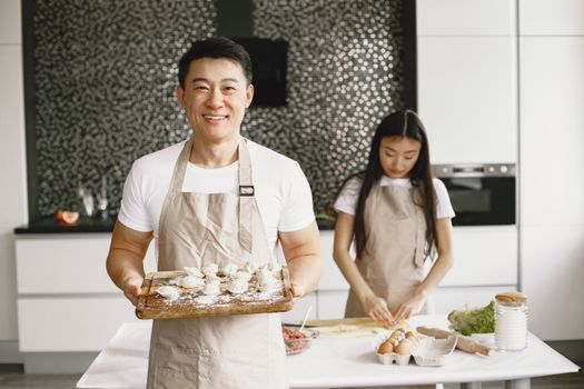 Asian couple making dumplings in a contemporary kitchen, smiling and enjoying their time together.