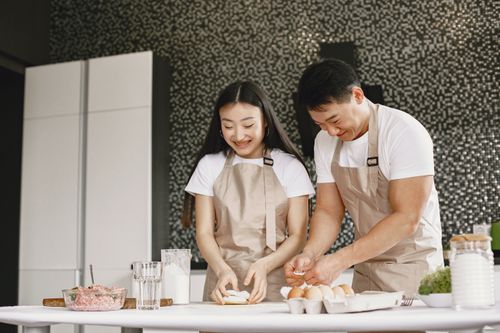Free Asian couple enjoying food preparation in a modern kitchen, smiling and having fun. Stock Photo