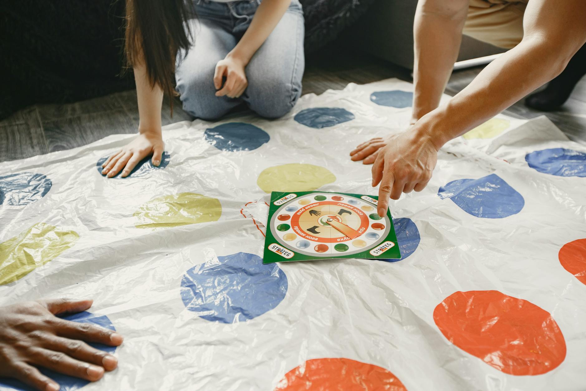 Hands on a colorful mat game with a spinner at the center. Fun and interactive play.