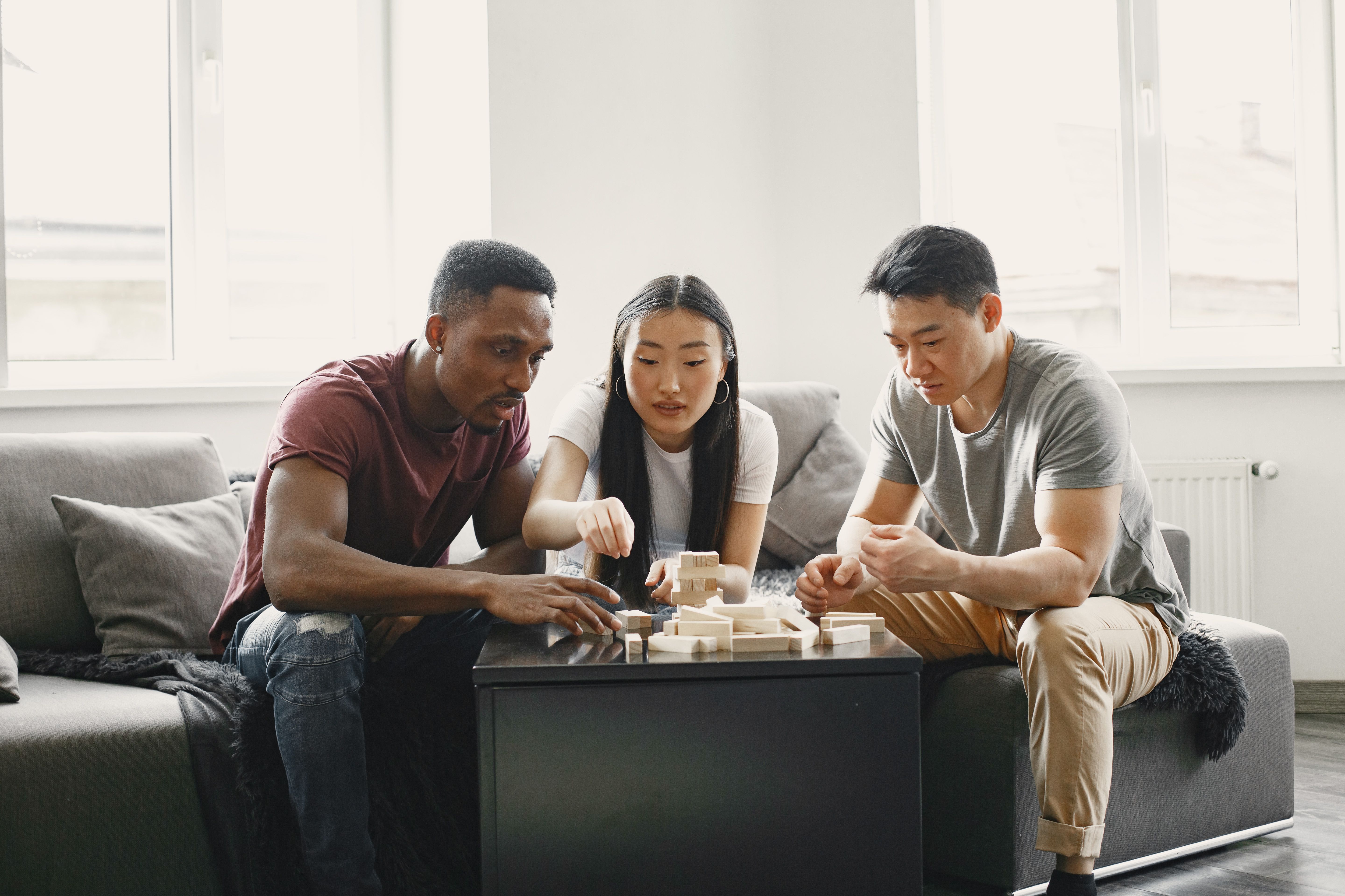 Three friends playing a wooden block game in a cozy living room setting.