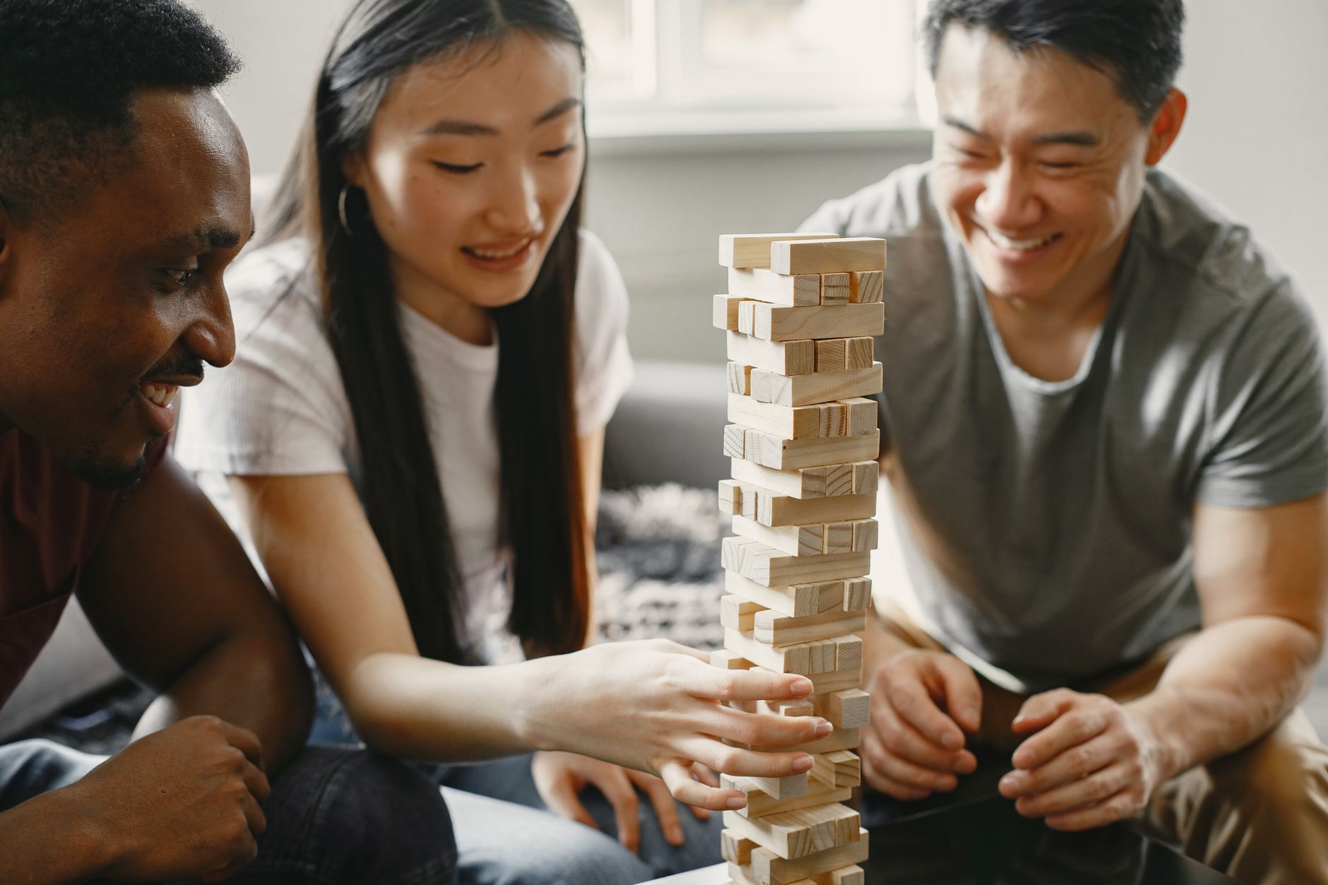 A diverse group enjoying a fun game of Jenga indoors, showcasing concentration and smiles.