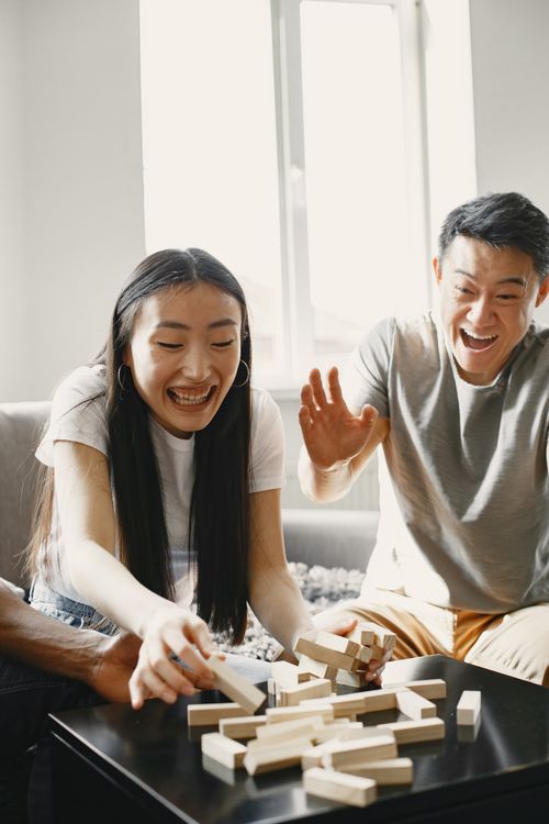 Free Friends enjoying a lively game of Jenga indoors, laughing and having fun. Stock Photo