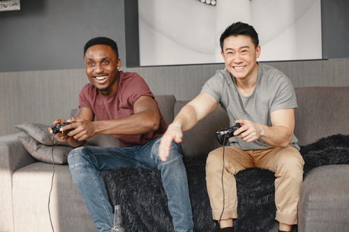 Free Two diverse friends laughing and playing video games together on a comfortable sofa. Stock Photo