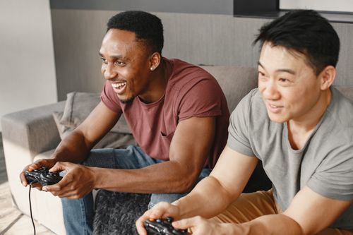 Free Two friends joyfully playing video games indoors on a cozy couch. Stock Photo