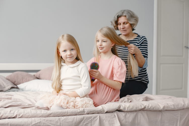 Girls Sitting On The Bed With Their Grandma While Touching Their Hair