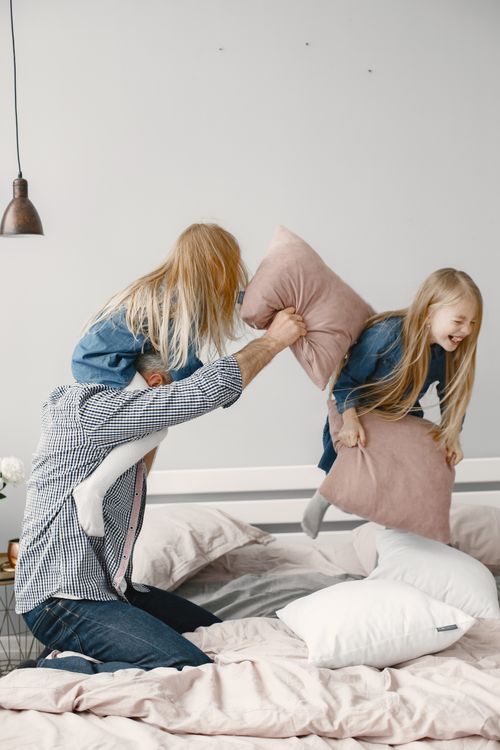 Free A joyful family bonding moment with a playful pillow fight in a cozy bedroom setting. Stock Photo