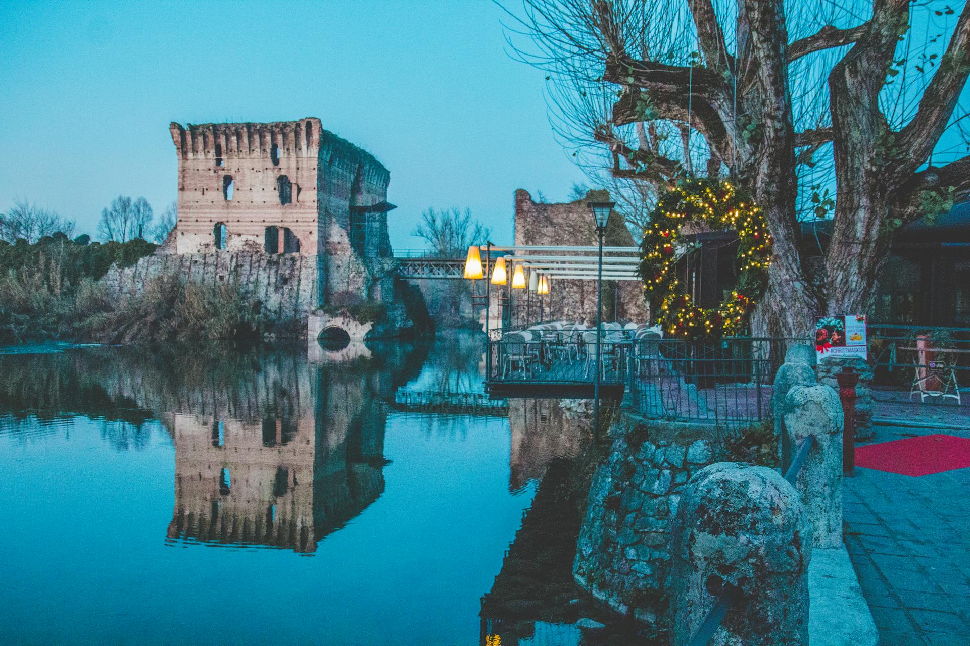 Calm and picturesque evening scene at Valeggio sul Mincio bridge, reflecting holiday lights on tranquil waters.