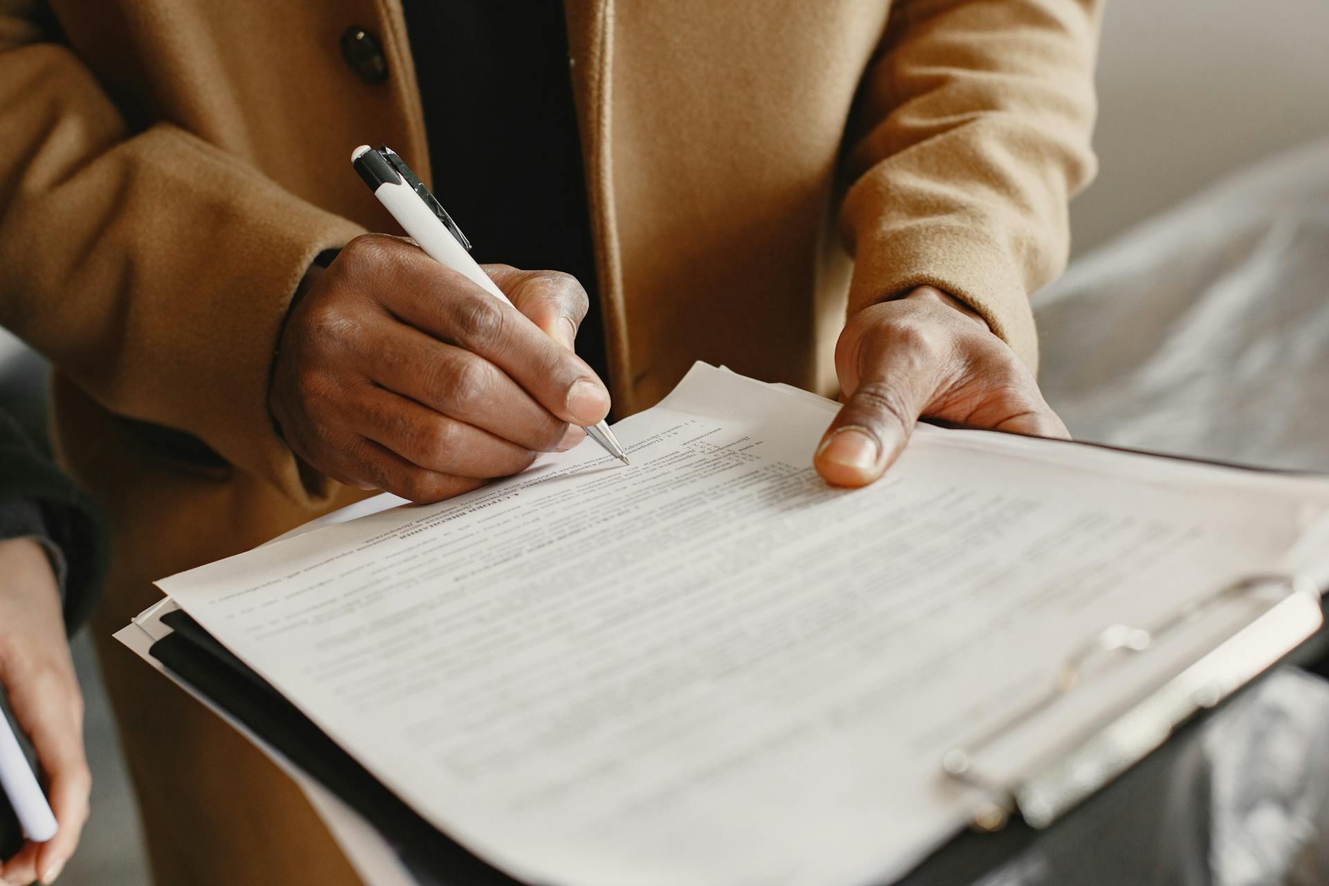 Close-up of a person signing a contract on a clipboard, focusing on legal formalities.