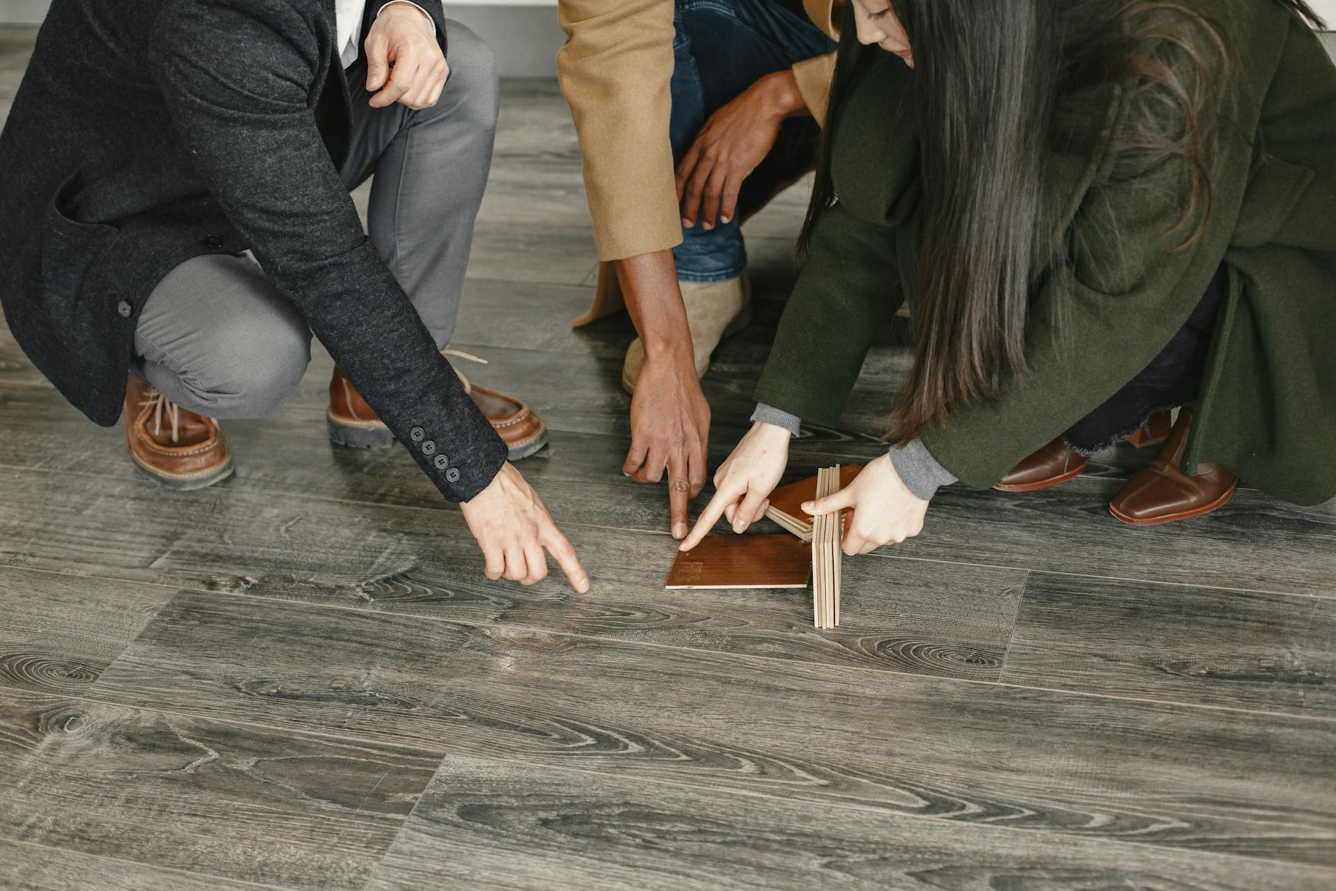 Three adults selecting flooring options indoors, focused on wooden samples and decision-making.