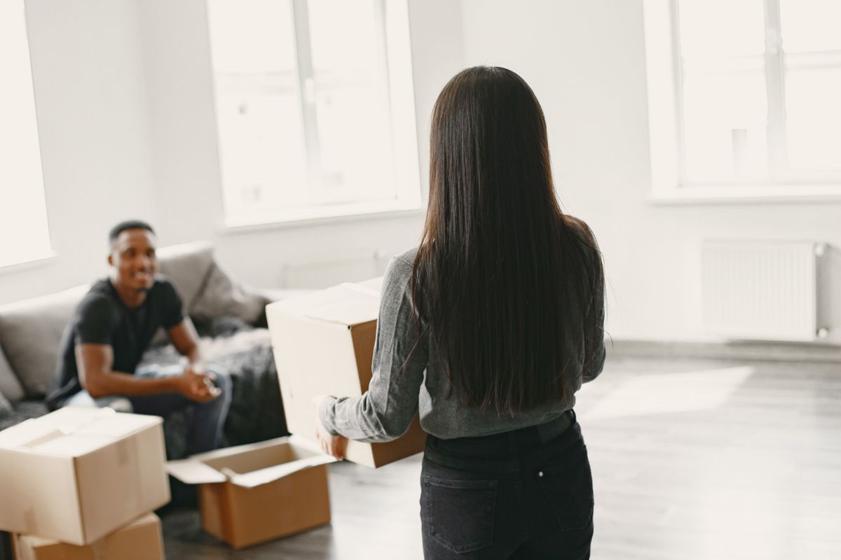 Two young roommates carrying moving boxes into their first apartment living room